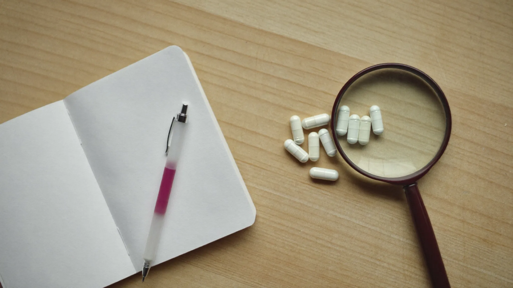 White dietary supplement capsules with a magnifying glass and notebook, representing an honest FemiPro bladder supplement review