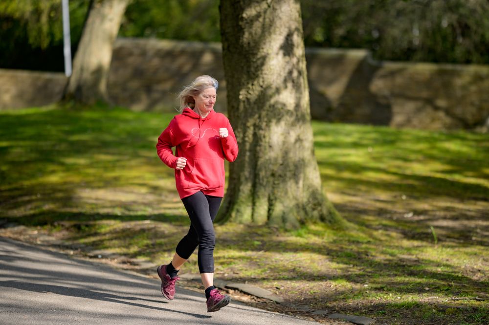 Active woman in her 50s jogging in a sunlit park — staying active supports bladder health after 45